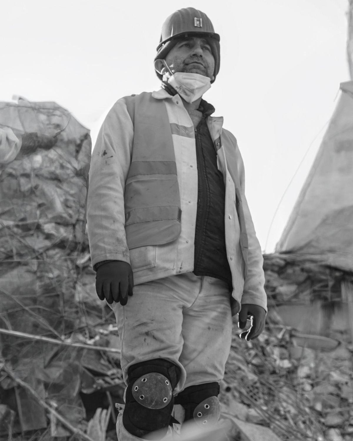 Black and white image of a person in hazmat gear standing in a pile of rubble after a natural disaster
