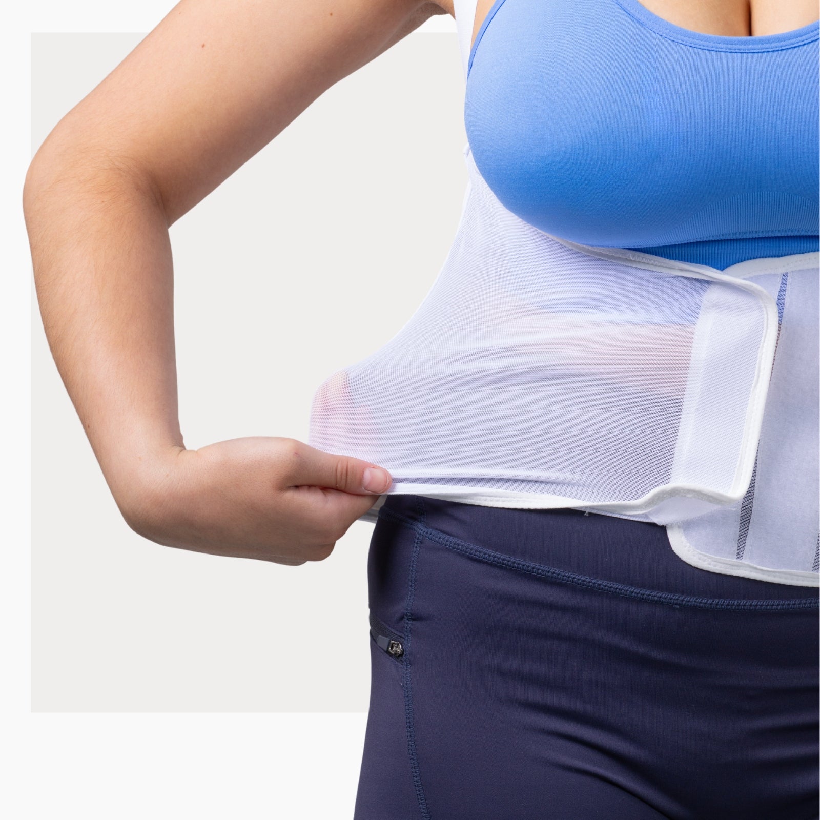 Woman wearing a white ThermApparel Cooling Vest pulling the breathable mesh out from her torso showing how stretchable and comfortable the cooling vest is. 